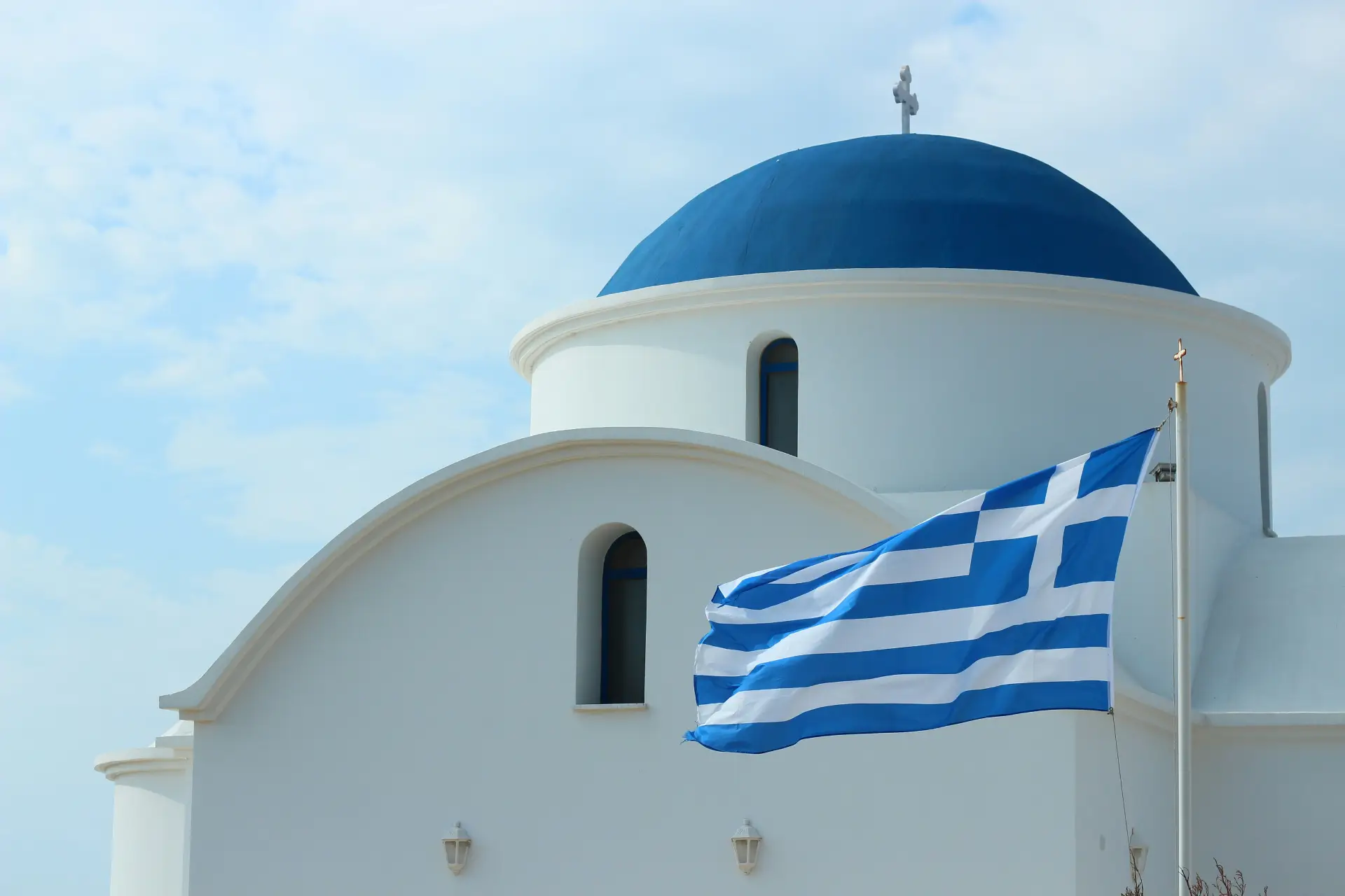 A white church with blue dome and the greek flag.
